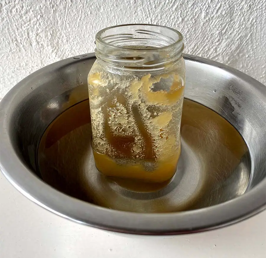 Open jar of cloudy honey inside a bowl of hot water