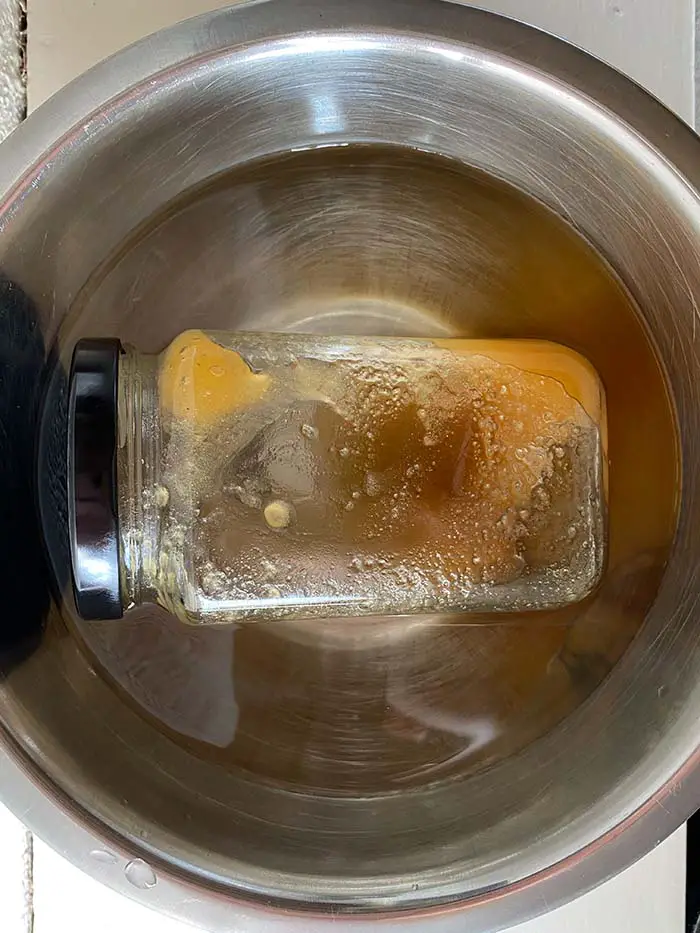 Closed jar of crystalized honey lying down in a bowl of warm water