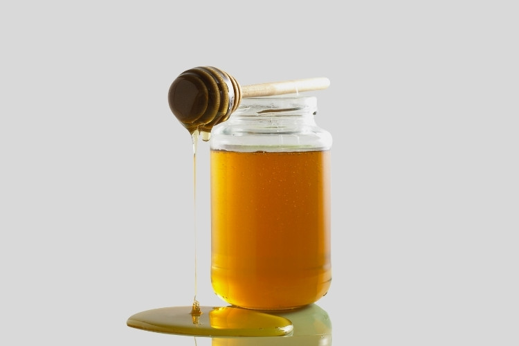 Jar of light honey with a wooden dipper in a grey background